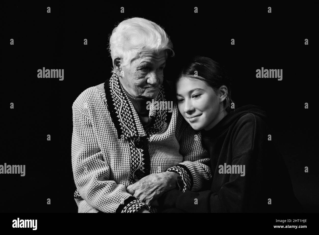 Ältere Frau, die mit einer erwachsenen Enkelin auf schwarzem Hintergrund sitzt. Schwarzweiß-Foto. Stockfoto