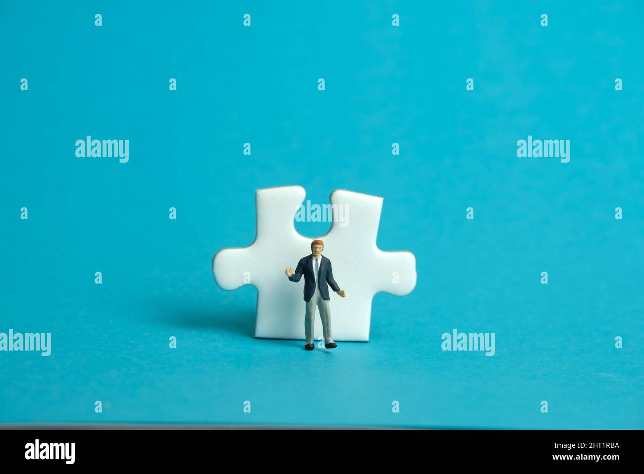 Miniatur Menschen Spielzeug Figur Fotografie. Ein schnupfender Geschäftsmann, der vor einem Puzzle-Puzzleteil steht. Isoliert auf blauem Hintergrund. Bildfoto Stockfoto