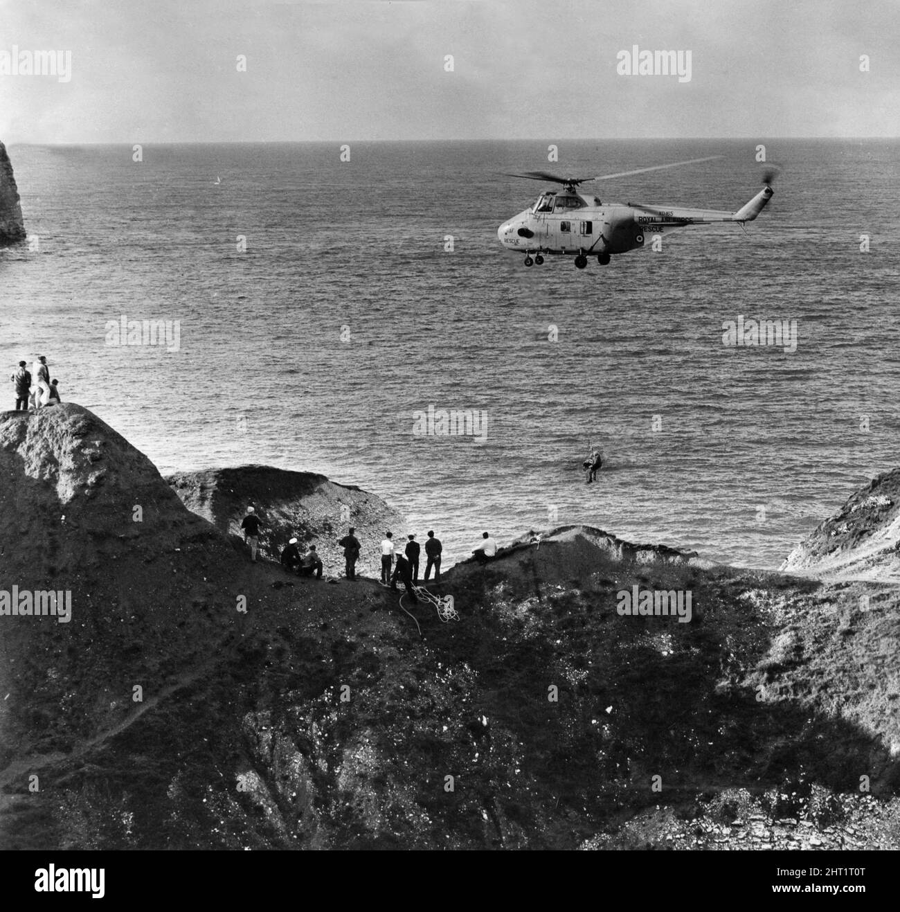 Urlauber beobachten, wie ein RAF-Wincher der verletzten Partei an Bord eines Westland Wirbelwind HAR10-Hubschraubers hilft, während er über den Klippen von Flamborough schwebt. 30.. August 1965 Stockfoto