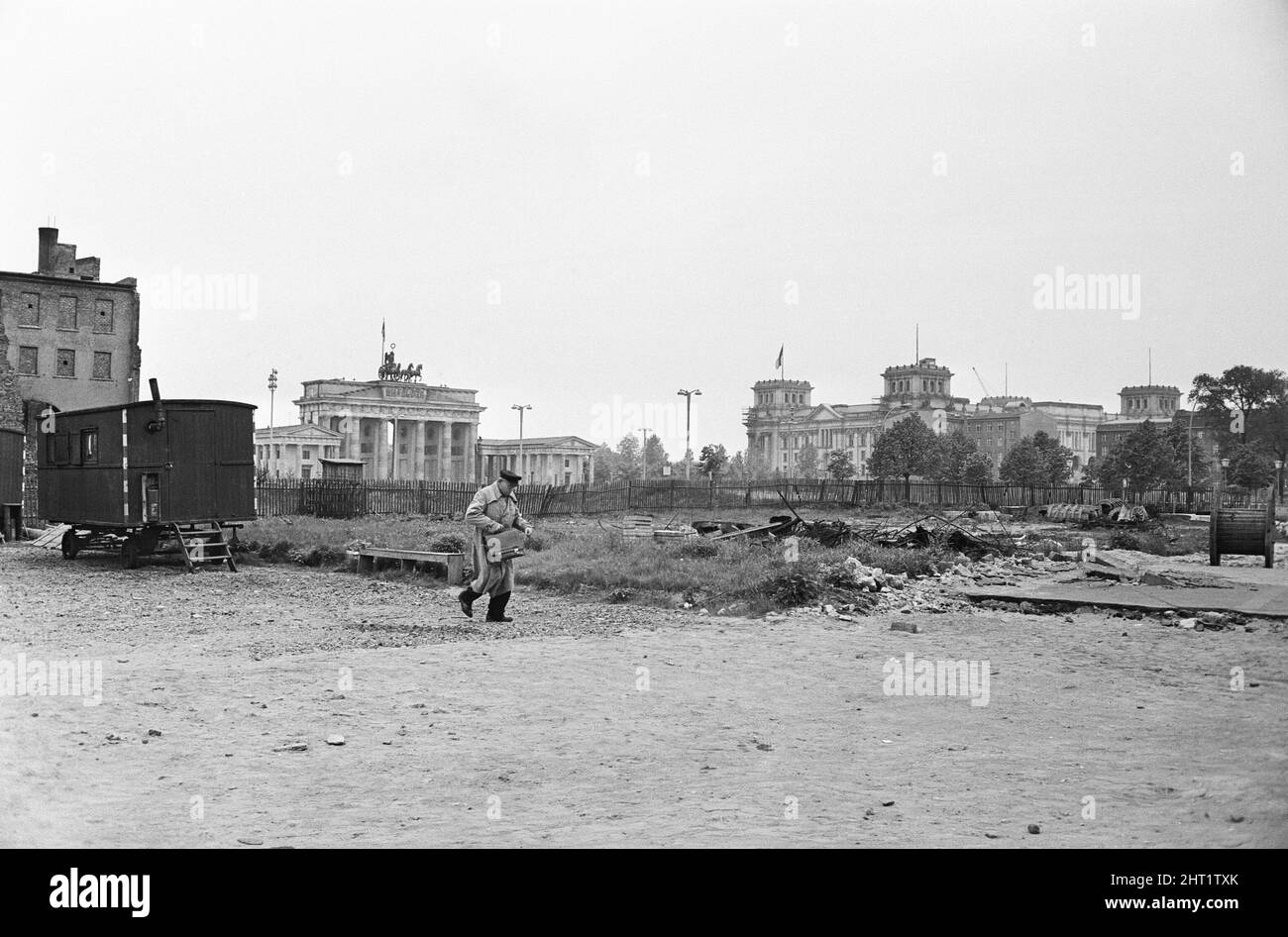 Szenen in Ost-Berlin, vier Jahre nach Beginn der Arbeiten am Bau der Berliner Mauer, die Ost und West trennt. Ein Mann, der durch eine heruntergekommene Gegend mit dem Brandenburger Tor und dem Reichstag im Hintergrund läuft. 26. Mai 1965. Stockfoto