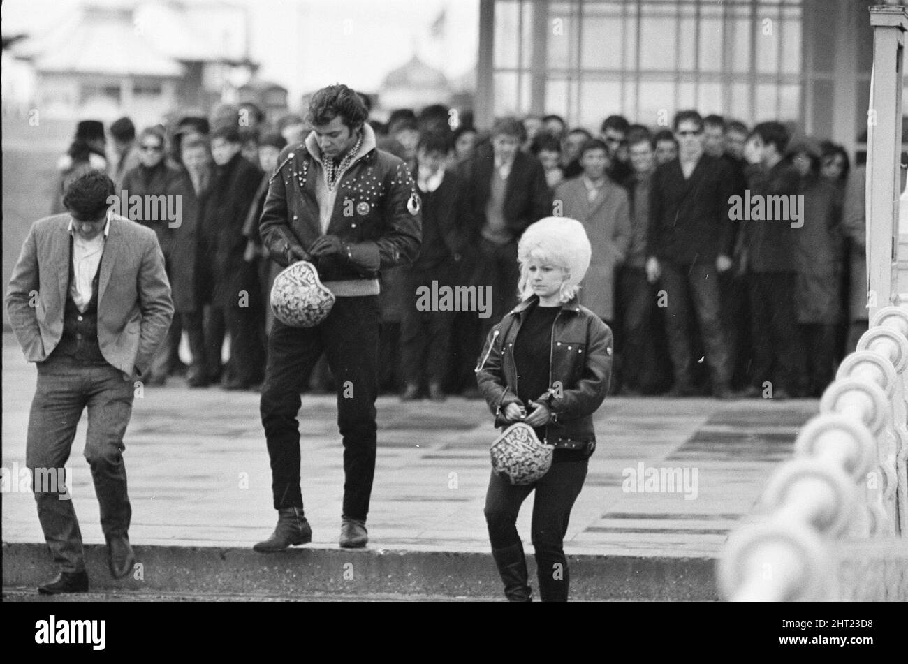 Die Mods und Rockers waren zwei widersprüchliche britische Jugendsubkulturen von Anfang bis Mitte 1960s. Die Berichterstattung über die Kämpfe von Mods und Rockern im Jahr 1964 löste eine moralische Panik über britische Jugendliche aus, und die beiden Gruppen wurden als Volksteufel bezeichnet. Mods im Hintergrund, 2 Rockers im Vordergrund bei Brighton. 18.. April 1965. Stockfoto