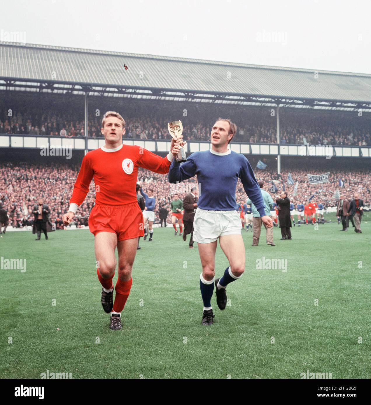 Das 1966 FA Charity Shield Merseyside Derby-Spiel zwischen Liverpool und Everton im Goodison Park. Vor dem Spiel haben Roger Hunt, Alan Ball und Ray Wilson die Weltmeisterschaft, den FA Cup und die Football League Trophy um den Goodison Park geführt. Liverpool gewann das Spiel mit einem Tor von 1 zu 0. Das Bild zeigt: Roger Hunt und Ray Wilson, Mitglieder des siegreichen England-Teams des Sommers, paradieren die WM-Trophäe um das Stadion. 13.. August 1966. Stockfoto