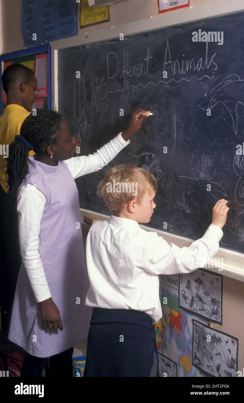Gruppe von drei multikulturellen Schulkindern, die auf einer Tafel im Klassenzimmer schreiben Stockfoto