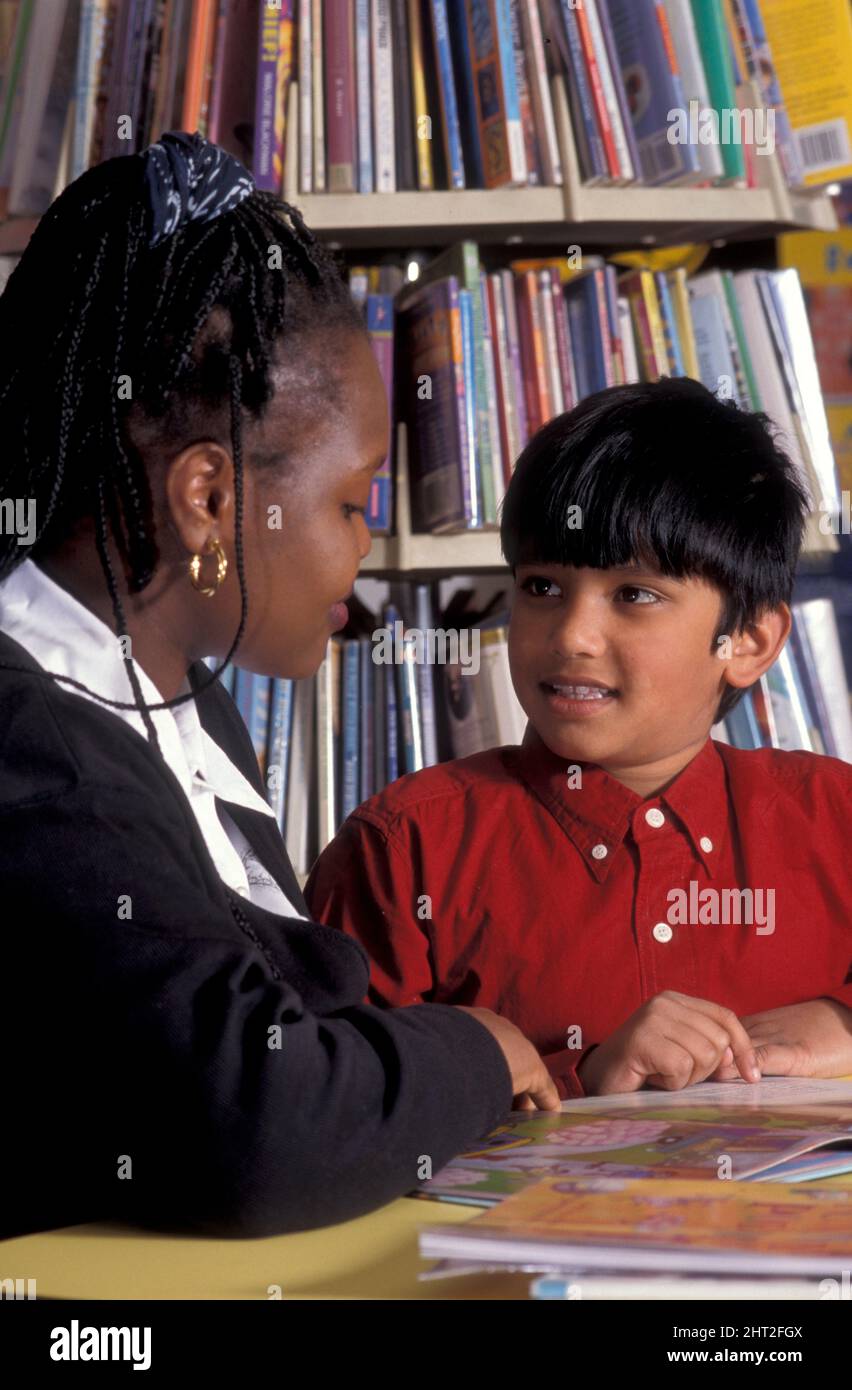 Afrikanische Frau beim Lesen mit asiatischem Jungen in der Bibliothek, die spezielle Bedürfnisse hat Stockfoto