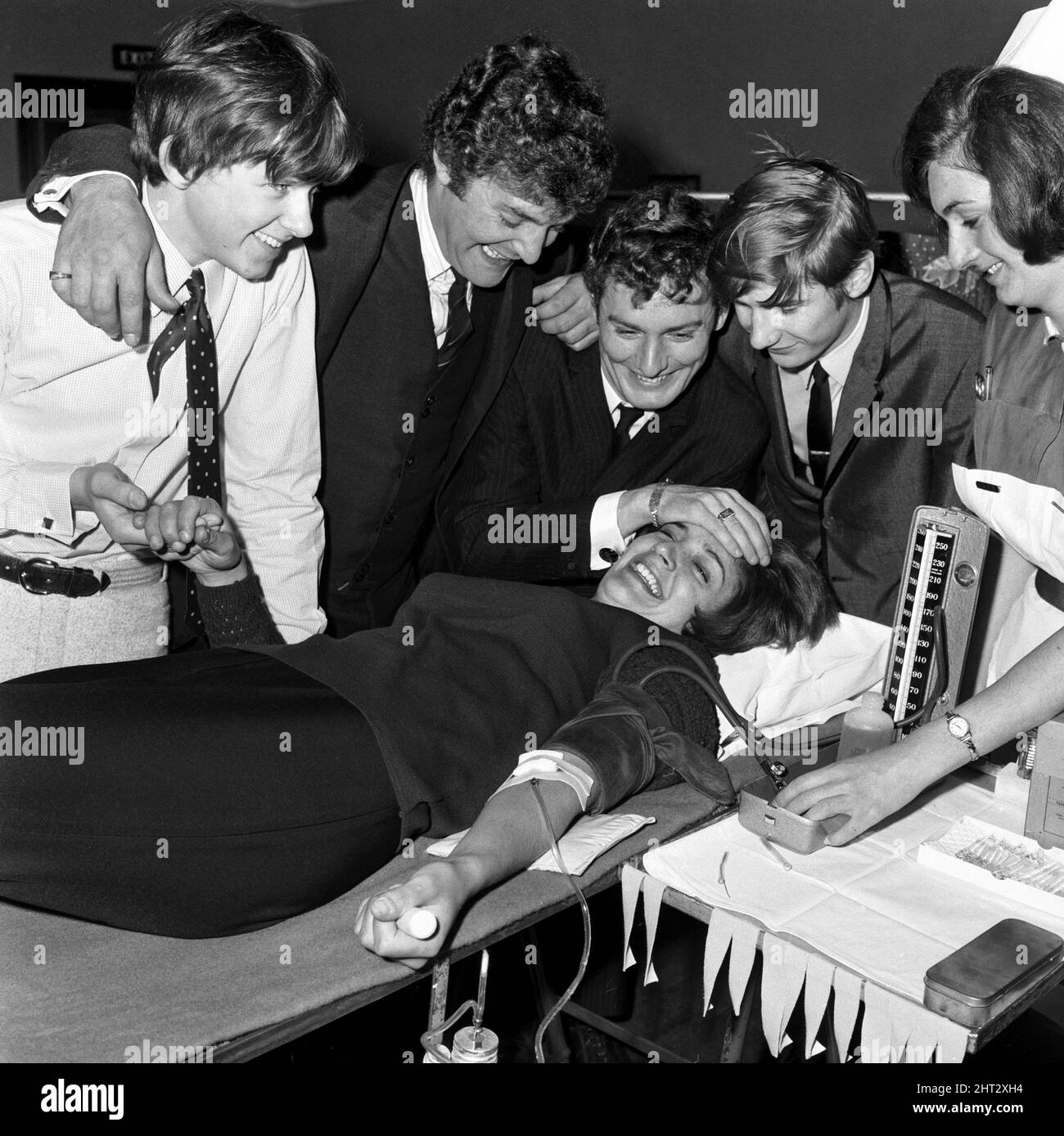 Die Popgruppe The Honeycombs hat auf den Aufruf des Gesundheitsministers zu mehr Blutspendern reagiert. Der Bluttransfusionsdienst wurde arrangiert, damit sie in ihre Aufnahmen passen. Die Jungs der Gruppe von links nach rechts: Alan ward, John Langtree, Peter Pye und Dennis Dell helfen dem Gruppenmitglied Honey Langtree auf der Couch zu trösten. Die Krankenschwester ist Sandra De Angelis September 1965 Stockfoto