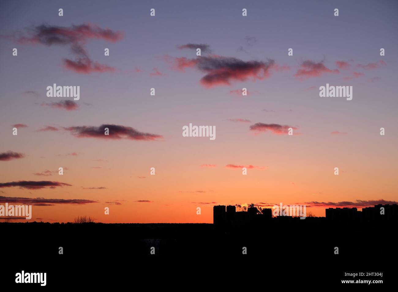 Landschaft, mit verstörendem roten Sonnenuntergang am Himmel und wenigen Wolken über dunkler Skyline und einigen Gebäudekonturen in der Ferne Stockfoto