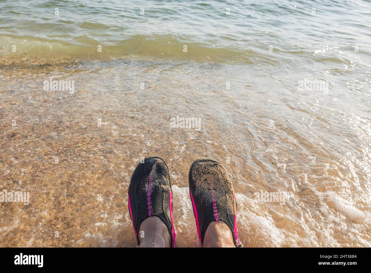 Wunderschöne Aussicht auf den Sandstrand und Badeschuhe auf den Füßen eines Mannes vor dem Hintergrund Meer. Griechenland. Stockfoto