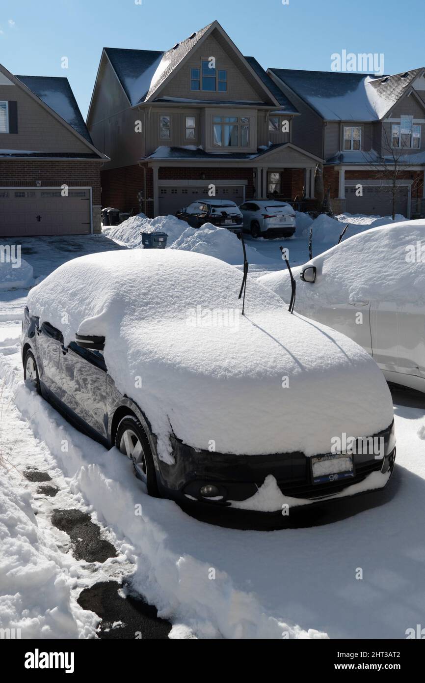 Einen halben Monat vor dem Frühjahr fiel wieder Schnee und bedeckte Autos parkten auf der Straße Stockfoto