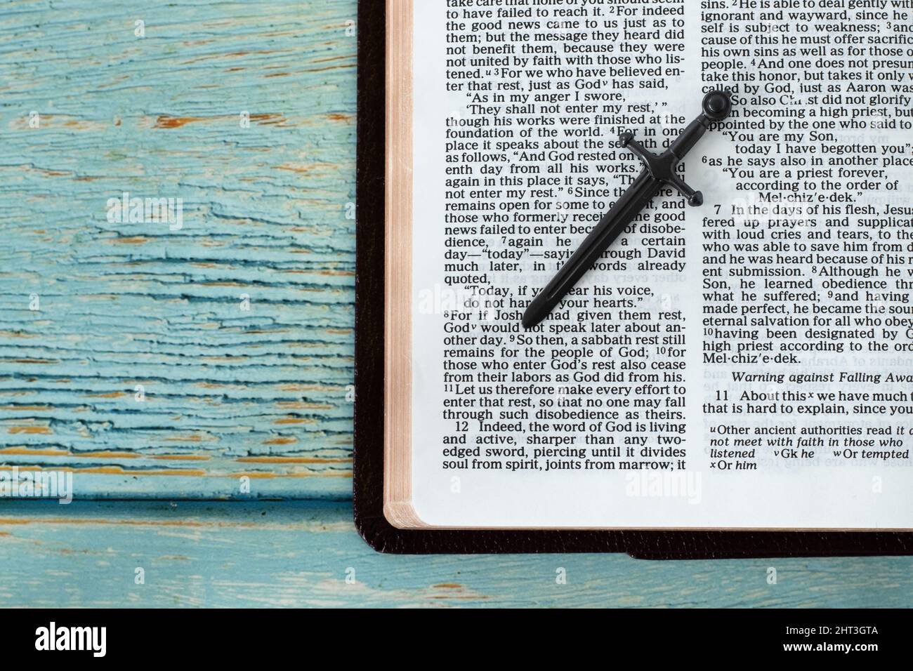Öffne das Heilige Bibelbuch mit einem Schwert auf blauem Holzhintergrund mit Kopierraum. Das biblische Konzept, das das Wort Gottes Jesus Christus studiert. Draufsicht. Stockfoto