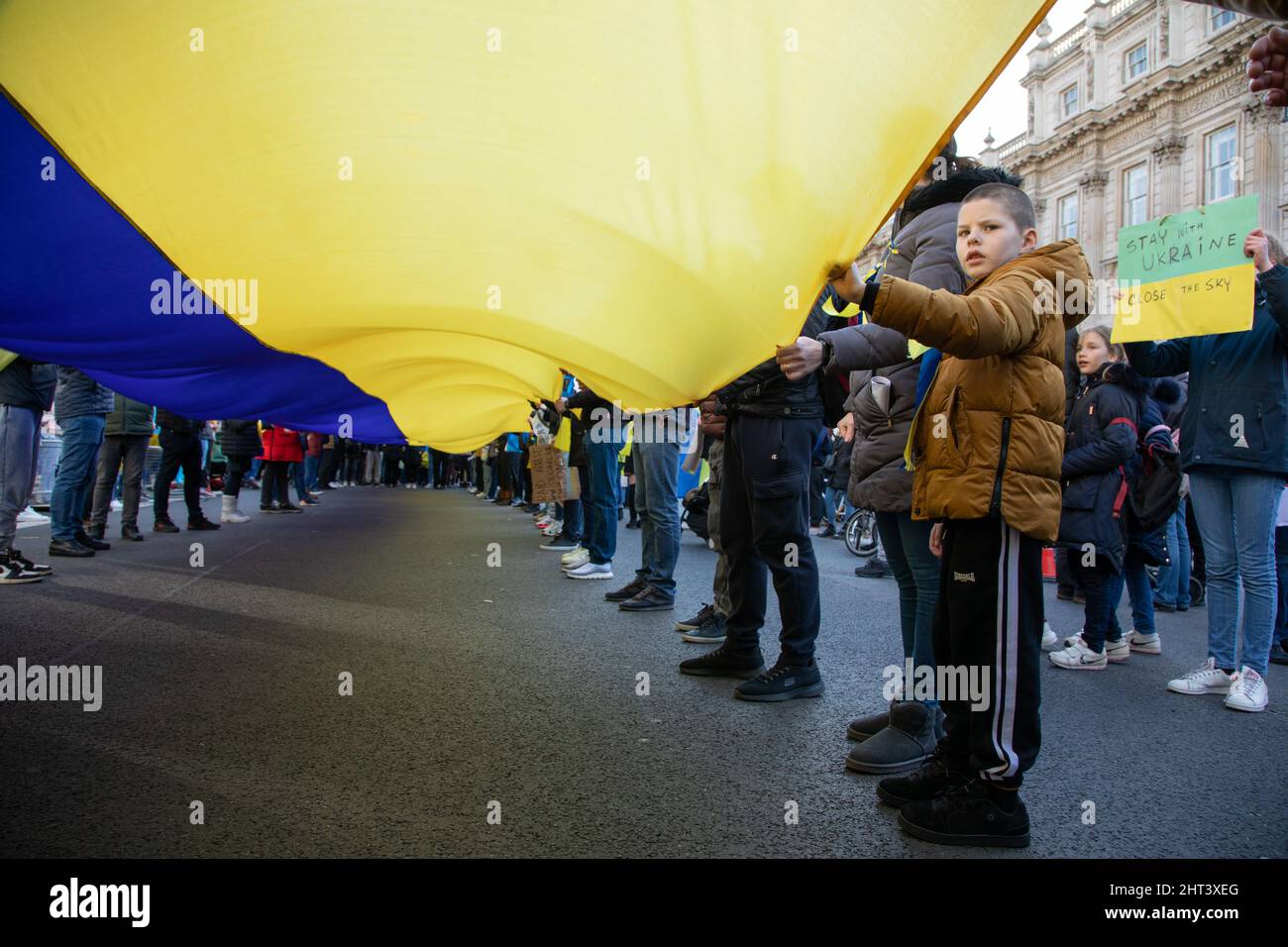 London, Großbritannien, 26.. Februar 2022 Ein Kind hält an einer riesigen ukrainischen Flagge fest, als sich Tausende in Whitehall versammelten, um gegen den jüngsten Angriff Russlands auf die Ukraine zu protestieren. Stockfoto