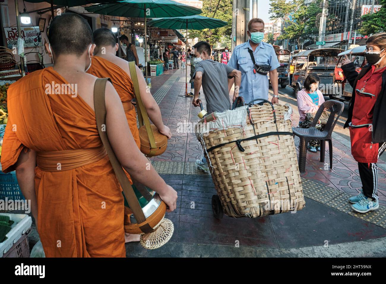Ein Marktarbeiter mit Trolley, ein Migrant aus Myanmar, eilt, um zwei buddhistischen Mönchen aus dem Weg zu gehen: Pak Klong Talat (Markt), Bangkok, Thailand Stockfoto