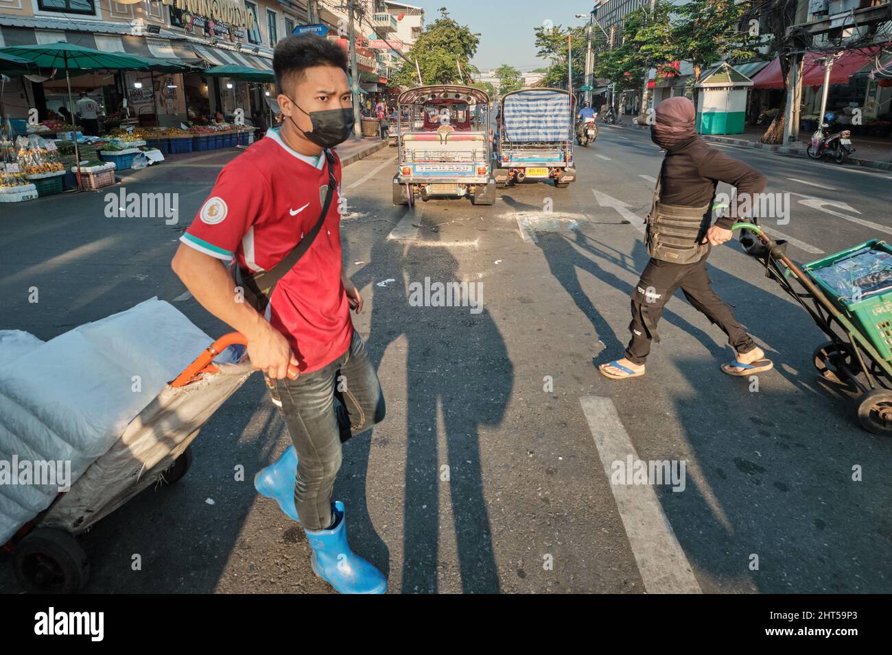 Zwei Marktmitarbeiter mit ihren Trolleys, Arbeitsmigranten aus Myanmar, stürzten über eine Straße in Pak Klong Talat (Markt), Bangkok, Thailand Stockfoto