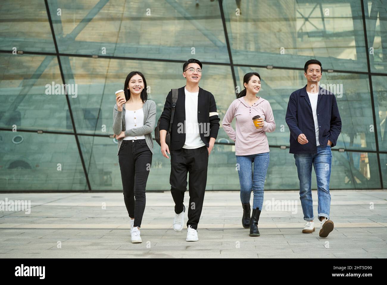 Eine Gruppe von vier jungen asiatischen Menschen, die sich unterhalten und auf der Straße in der modernen Stadt fröhlich und lächelnd spazieren gehen Stockfoto