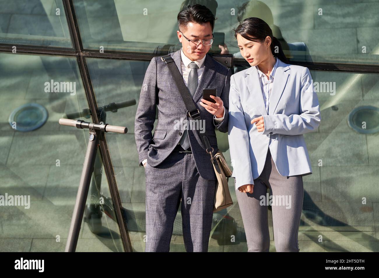 Junger asiatischer Geschäftsmann und junge Frau stehen draußen und blicken gemeinsam auf das Mobiltelefon Stockfoto