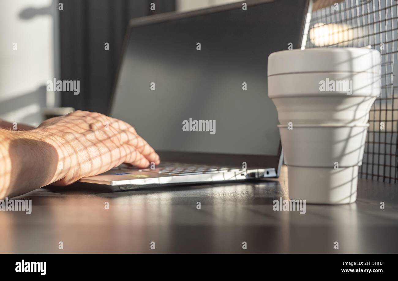 Mann Hände Nahaufnahme tippen auf Laptop-Tastatur. Geschäftsmann oder Student sitzen am Tisch mit Computer und eco Silikon Tasse zum Mitnehmen und arbeiten oder studieren. Hochwertige Fotos Stockfoto