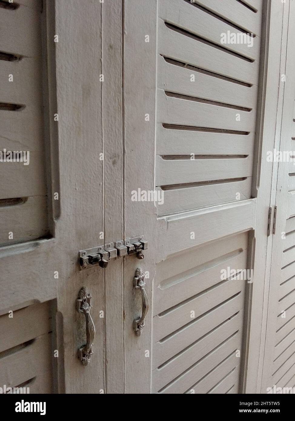Weißer Kleiderschrank mit geschlossenen Türen und Metallgriffen im Zimmer Stockfoto