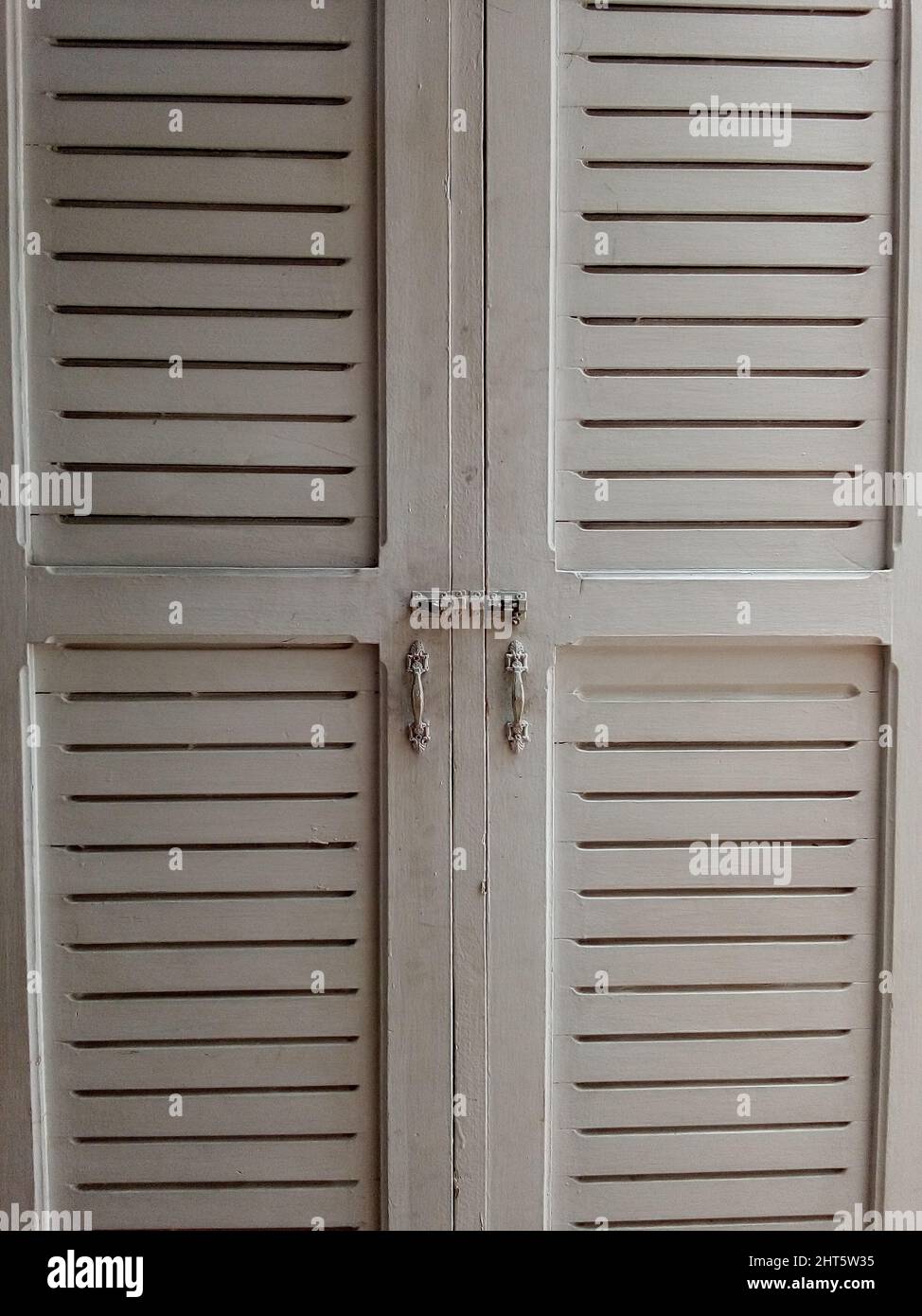 Weißer Kleiderschrank mit geschlossenen Türen und Metallgriffen im Zimmer Stockfoto