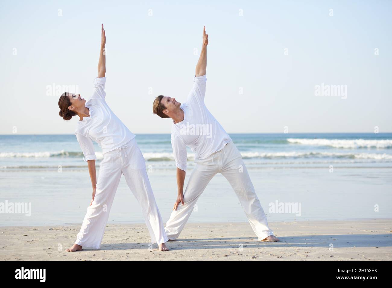 Yoga am Meer. Ein junges Paar, das am Strand Yoga praktiziert. Stockfoto