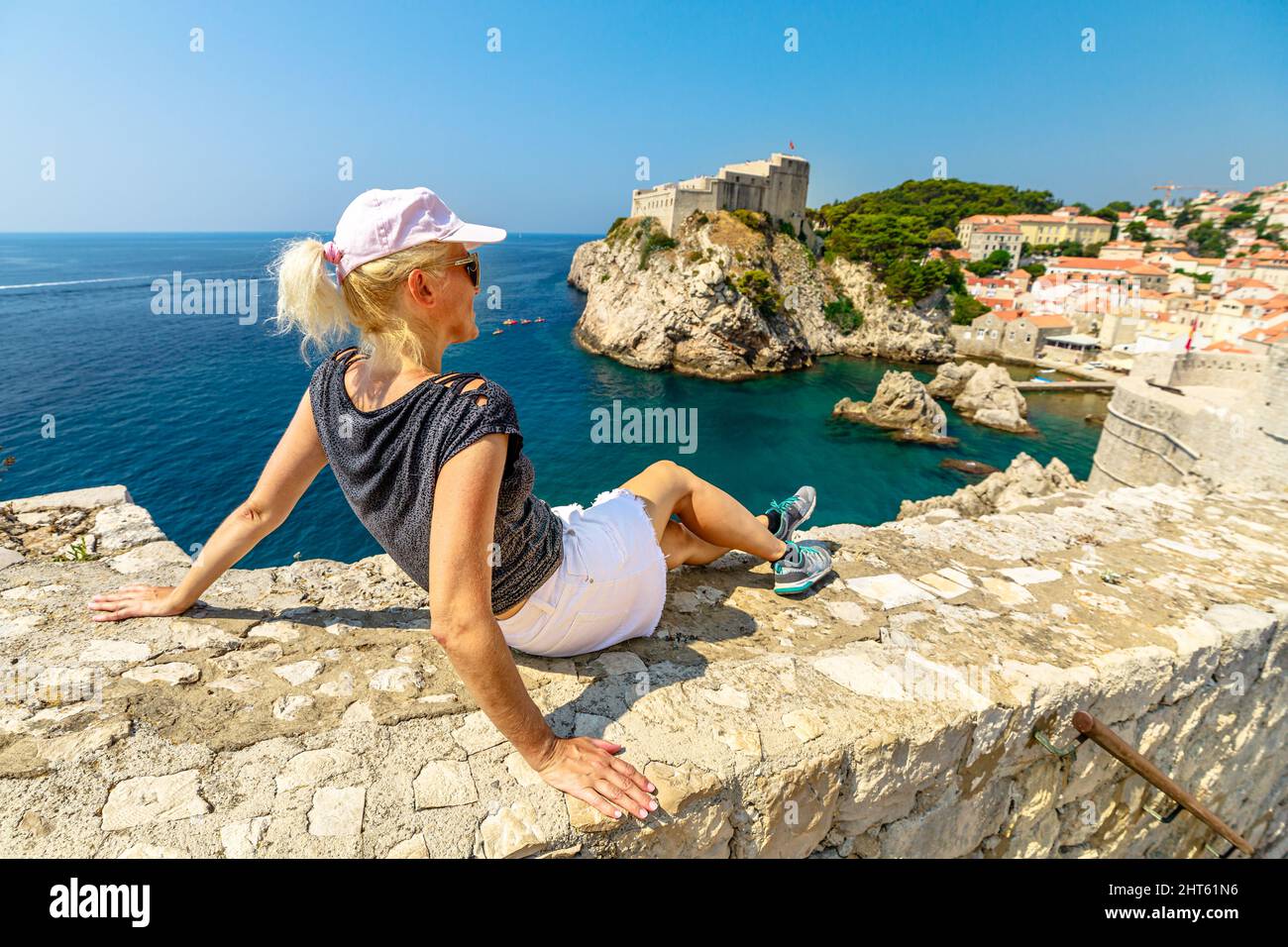 Frau an den oberen Wänden der Stadt Dubrovnik in Kroatien. Blick auf die Festung Fort Lovrijenac, über den Westhafen. Dubrovnik historische Stadt Kroatien in Stockfoto