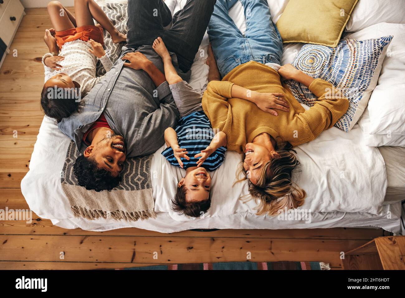 Blick von oben auf eine glückliche Familie, die zu Hause auf dem Bett liegt. Fröhliche Familie lächelt, während sie sich am Wochenende zusammen entspannen. Mama und Papa, die Qualität ausgeben Stockfoto