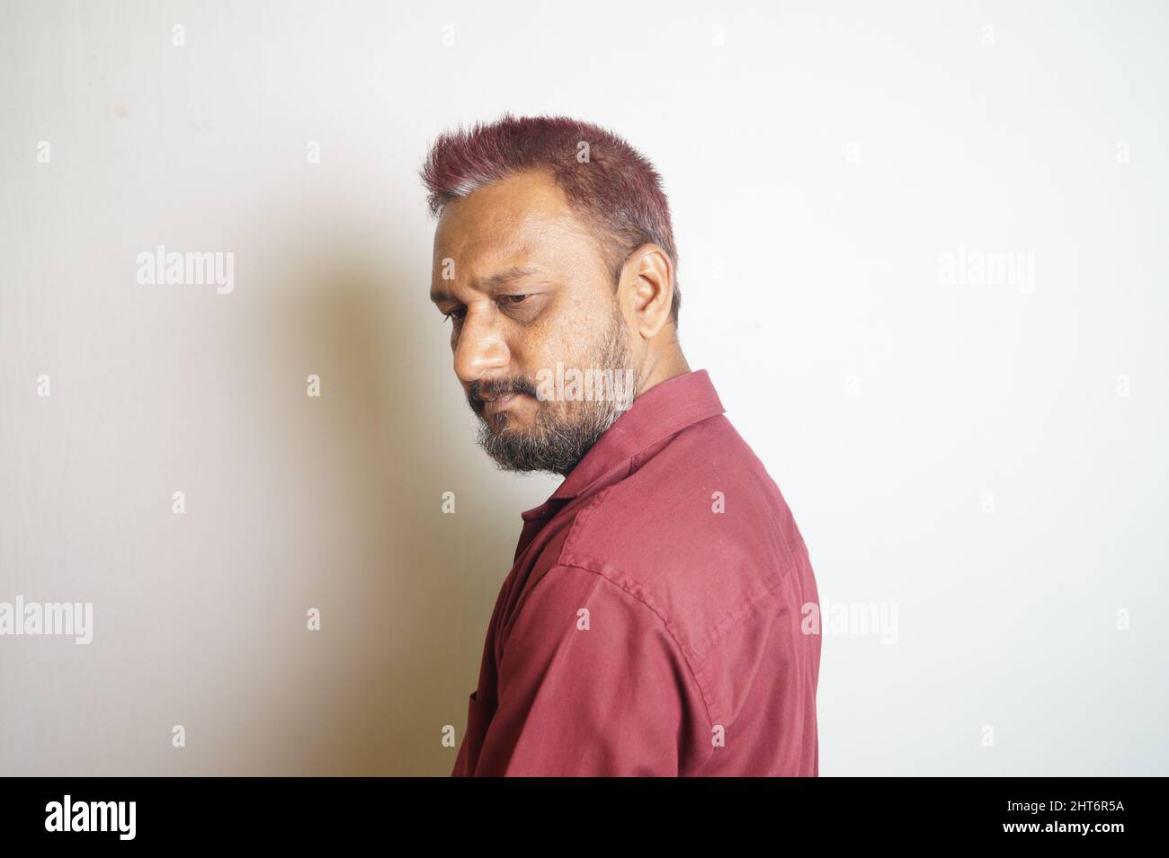 Ein bärtiger indischer Mann, der ein rotes Hemd auf weißem Hintergrund trägt Stockfoto