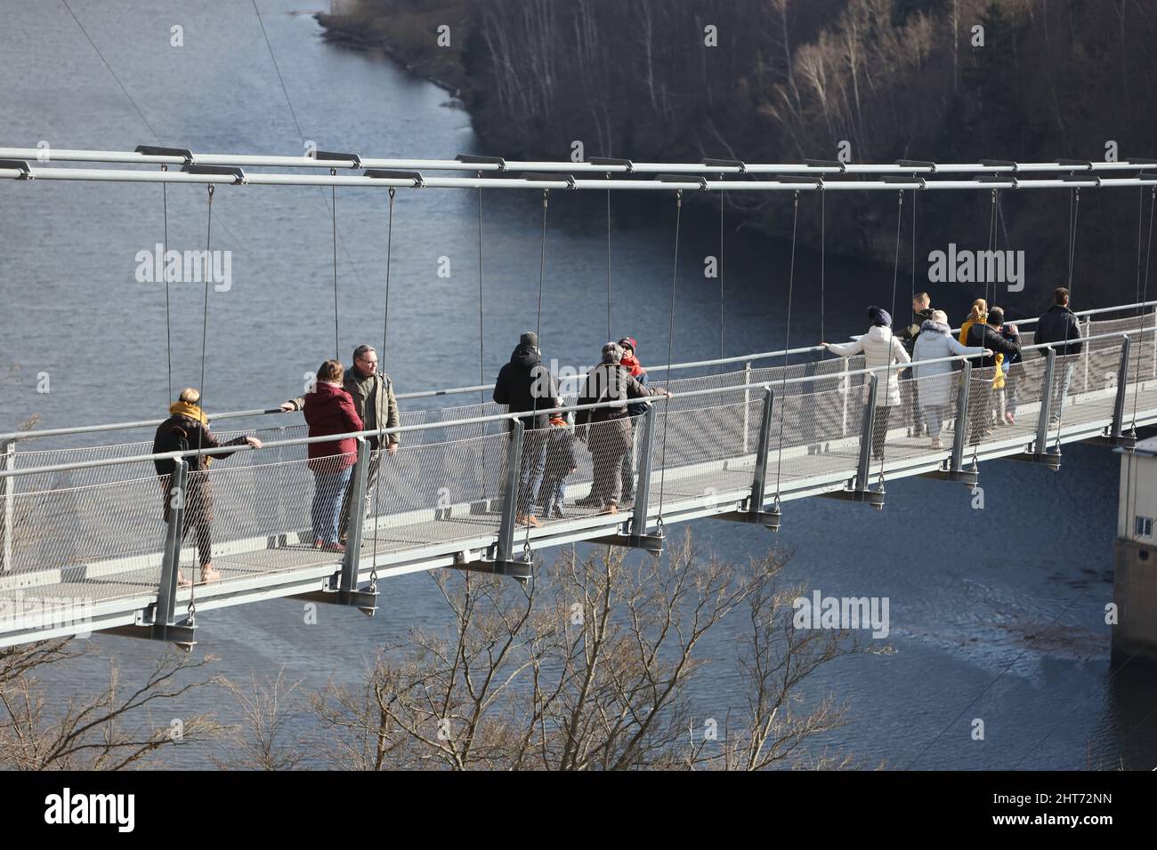 Hasselfelde, Deutschland. 27.. Februar 2022. Besucher laufen bei strahlendem Sonnenschein über eine Hängebrücke am Rappbode-Staudamm bei Hasselfelde. Die über 450 Meter lange Hängebrücke verläuft parallel zur höchsten Staumauer Deutschlands entlang des Rappbode-Staudamms. Quelle: Matthias Bein/dpa-Zentralbild/ZB/dpa/Alamy Live News Stockfoto