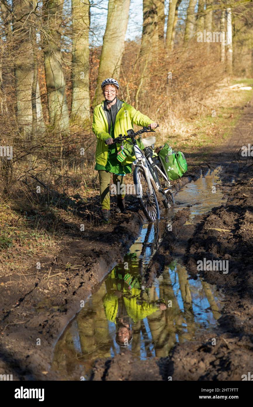 Frau über fünfzig macht mit ihrem E-Bike eine Radtour auf einem schlammigen Weg und durch Pfützen, Lüneburg, Niedersachsen, Deutschland Stockfoto