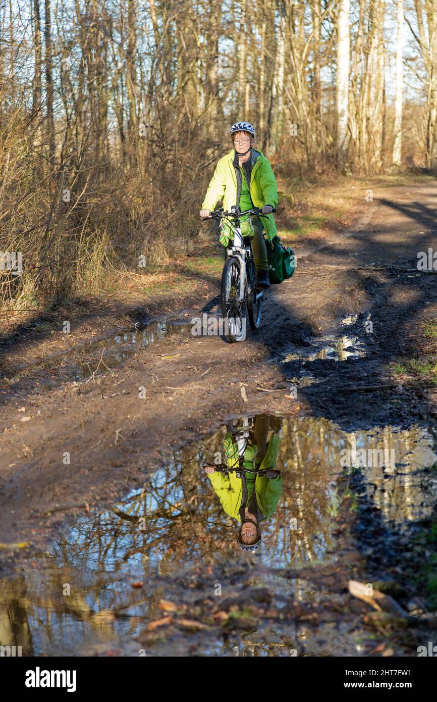 Frau über fünfzig macht mit ihrem E-Bike eine Radtour auf einem schlammigen Weg und durch Pfützen, Lüneburg, Niedersachsen, Deutschland Stockfoto