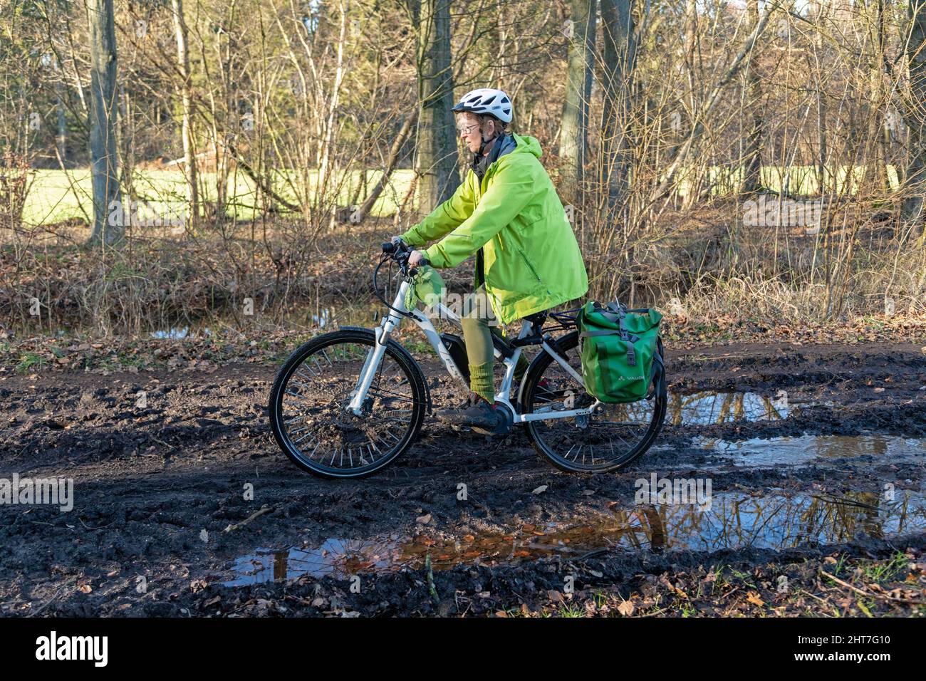 Frau über fünfzig macht mit ihrem E-Bike eine Radtour auf einem schlammigen Weg und durch Pfützen, Lüneburg, Niedersachsen, Deutschland Stockfoto