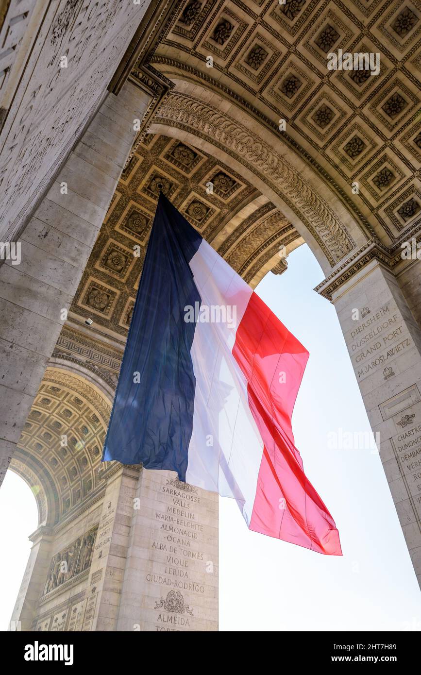 Niedrige Ansicht einer großen französischen Flagge, die unter dem Gewölbe des Triumphbogens in Paris, Frankreich, im Wind flattert. Stockfoto