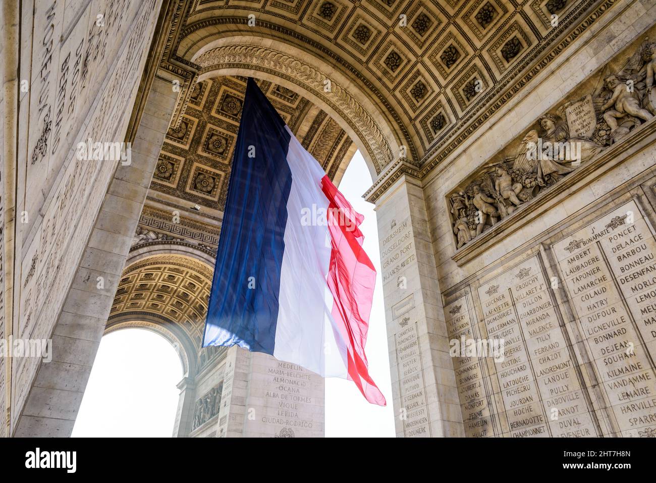 Niedrige Ansicht einer großen französischen Flagge, die unter dem Gewölbe des Triumphbogens in Paris, Frankreich, im Wind flattert. Stockfoto