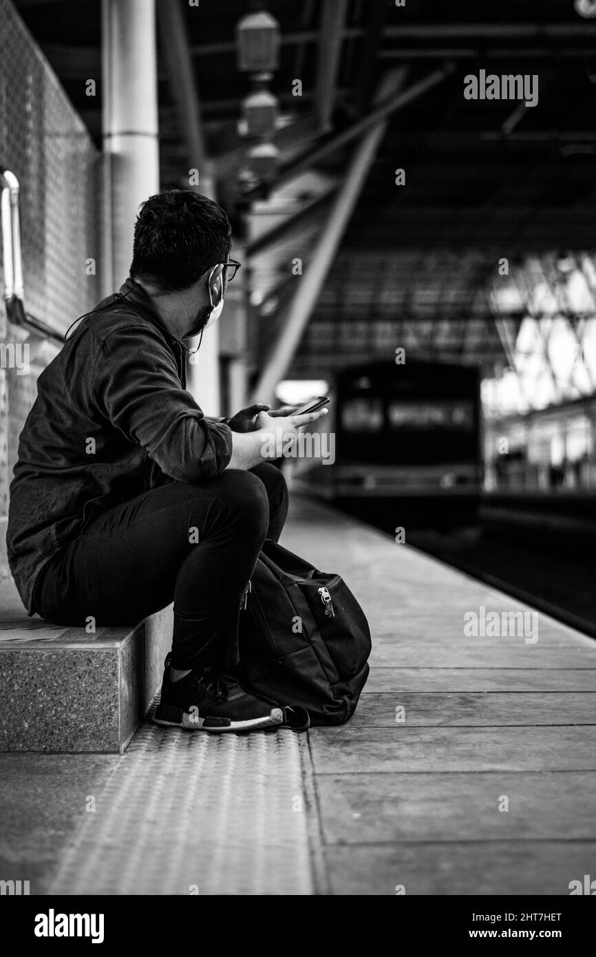 Eine vertikale Aufnahme eines Mannes, der in Schwarz-Weiß auf seinen Zug wartet Stockfoto