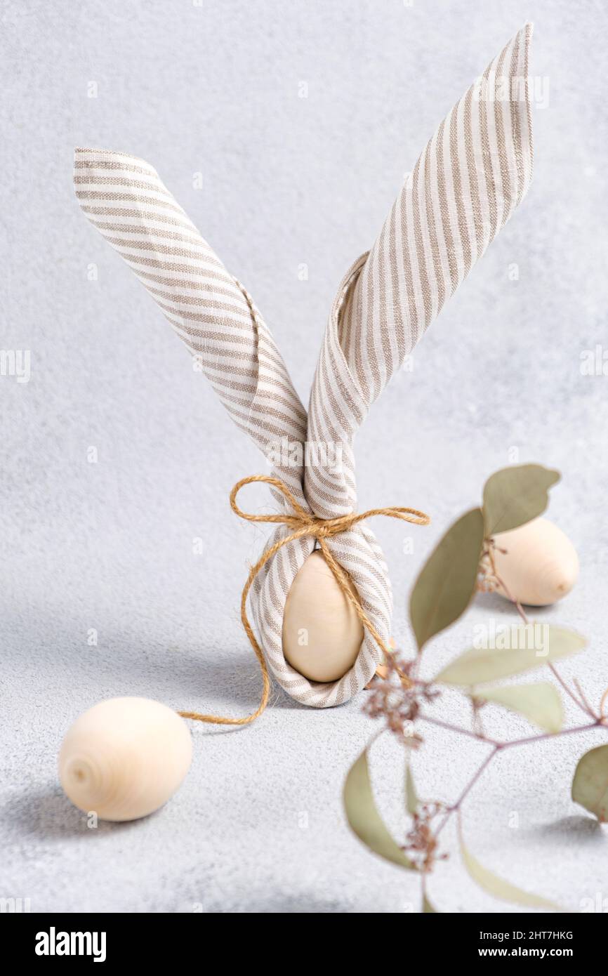 Ostereier in Leinenserviette in Form von Hase mit Ohren, Olivenzweig eingewickelt. Osterdekor in Pastelltönen auf grauem strukturiertem Hintergrund. Traditionell Stockfoto