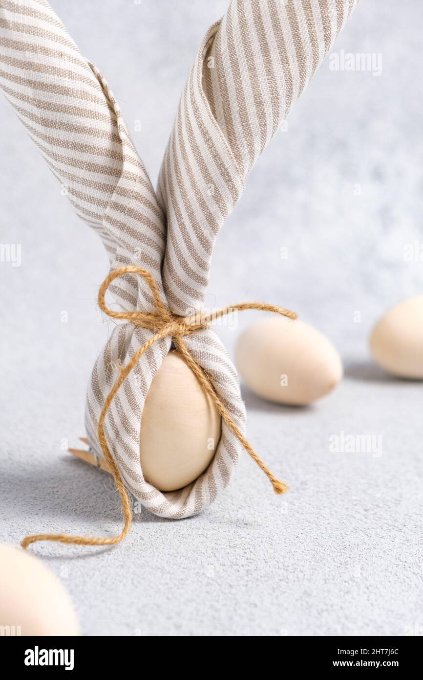 Nahaufnahme des Osterhasen aus Ei- und Leinenstreifen-Serviette. Ostereier sind hellbeige auf hellgrauem Hintergrund. Trend der traditionellen Dekoration Stockfoto