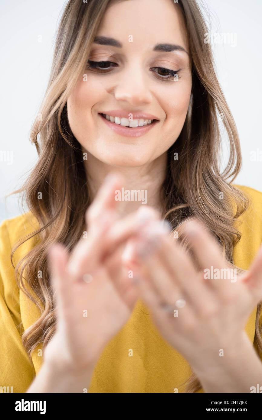Junge Brünette Frau verwendet kosmetische Creme, Blick auf ihre Hände Stockfoto