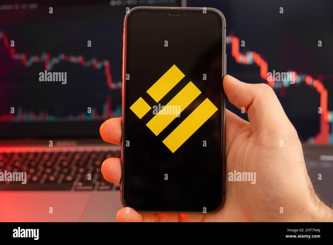 Binance USD BUSD Kryptowährung Logo auf dem Bildschirm des Smartphones in Mans Hand mit Abwärtstrend auf dem Chart auf rotem Hintergrund, Februar 2022, San Francisco, USA. Stockfoto