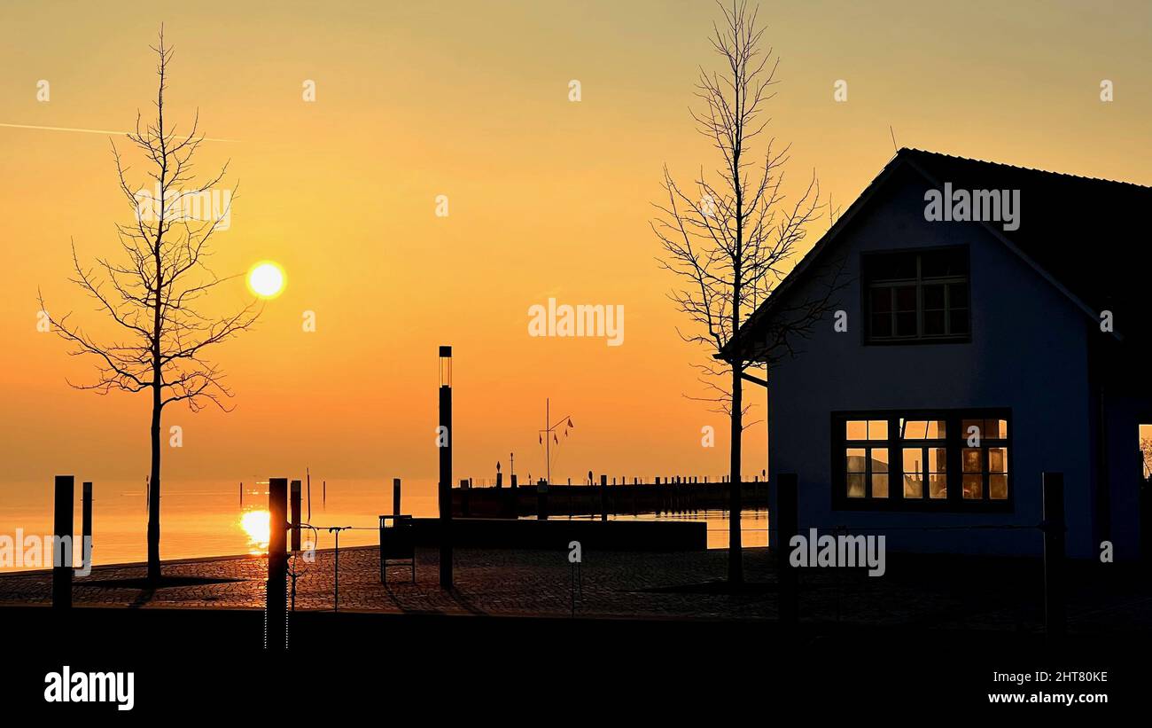 Szenischer Abendblick auf ein kleines Gebäude neben einem Gewässer vor einem orangefarbenen Himmel Stockfoto