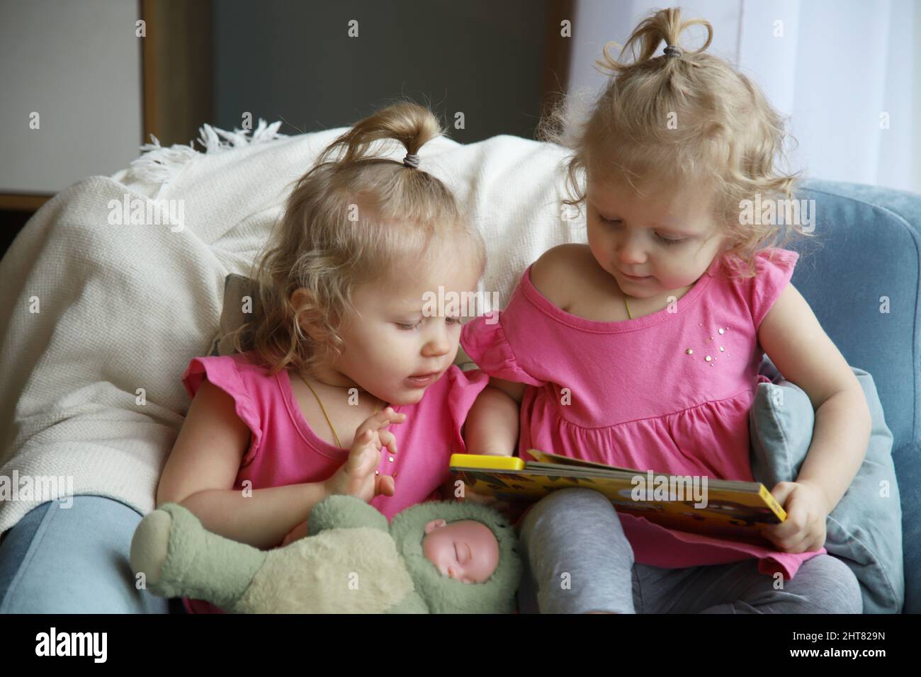 Zwillinge sitzen auf einem Stuhl und schauen sich ein Buch an Stockfoto