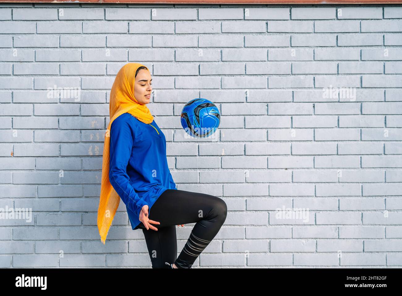 Ethnische Frau, die den Ball mit dem Knie in der Nähe der Ziegelmauer kickte Stockfoto
