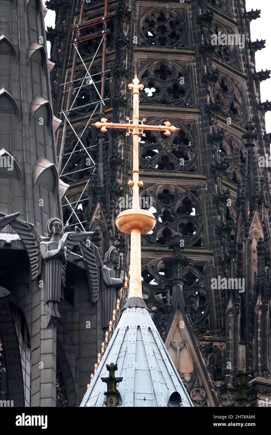 Köln, Deutschland - Feb 25 2022 Der Kölner Dom. Goldenes Kreuz auf dem Dach des Kölner Doms gegen einen verdunkelten Turm mit modernen Engeln Stockfoto