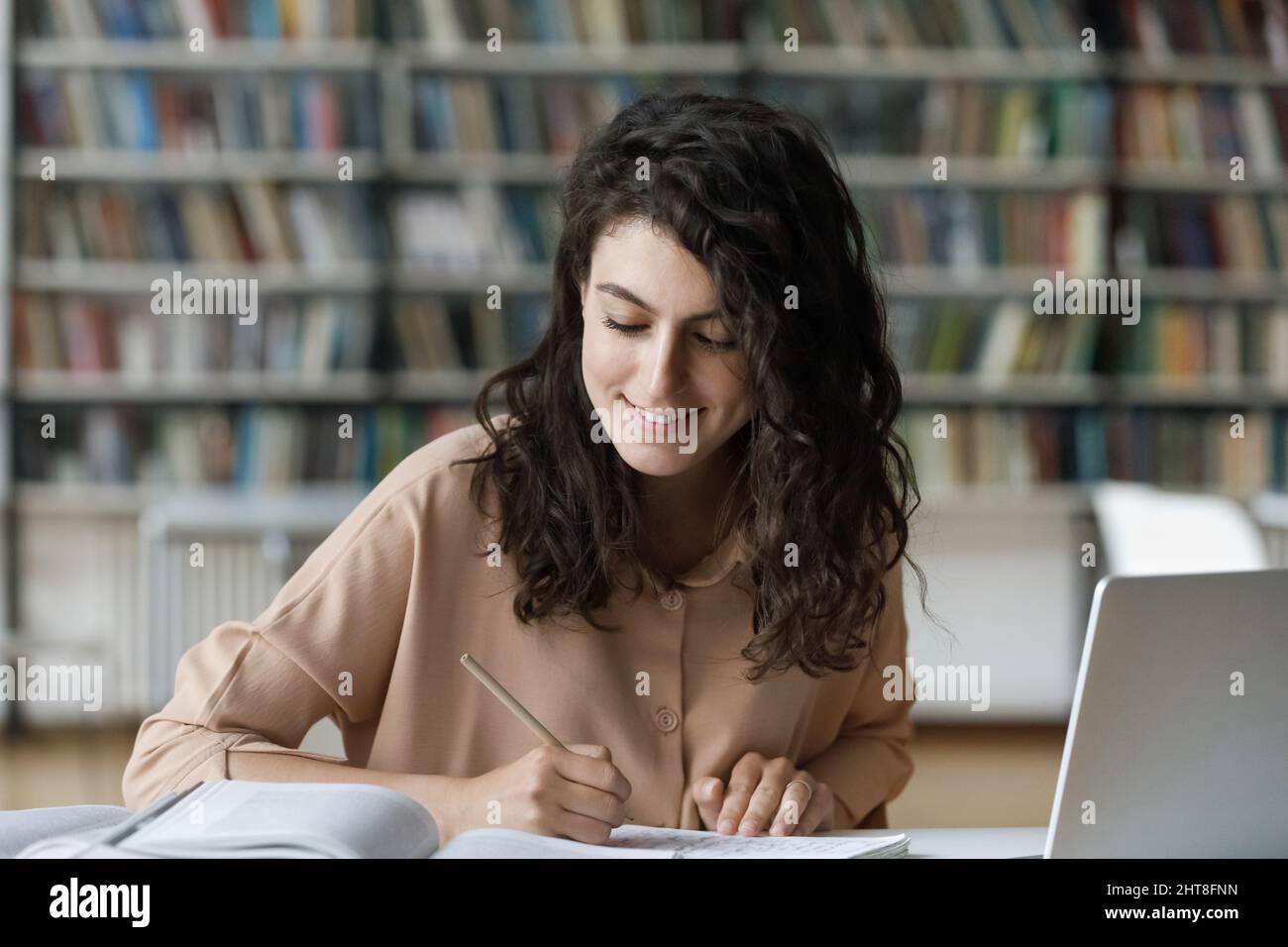 Glückliche junge hispanische Frau, die in der Bibliothek studiert. Stockfoto