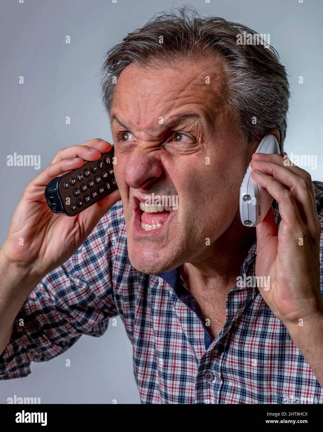 Ein weißer Mann brüllt, während er zwei schnurlose Telefone hält, mit einem Ausdruck von großem Stress Stockfoto