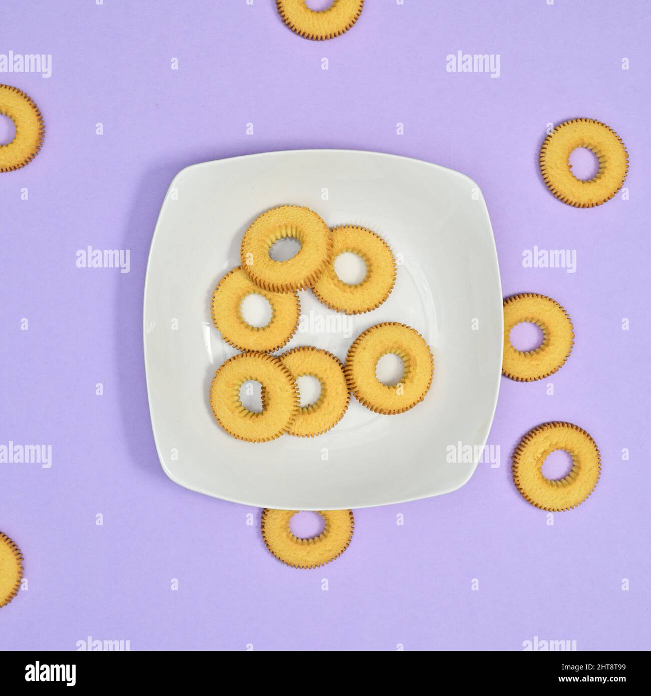 Kreative Plätzchen in weißem Teller auf pastellviolettem Hintergrund. Flat-Lay-Food-Konzept Stockfoto