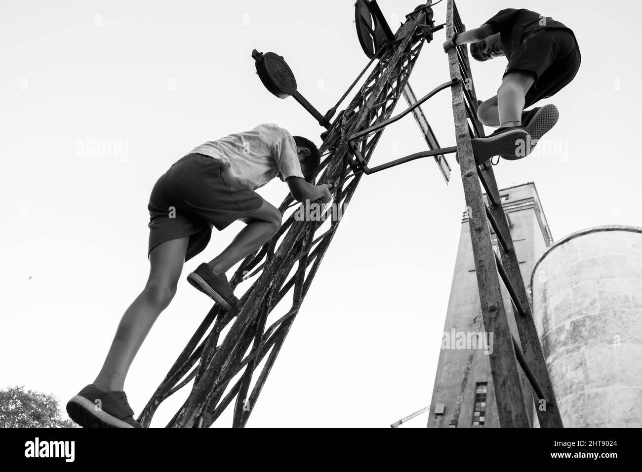 Low-Angle-Graustufenaufnahme von zwei jungen Männern, die einen Metallturm hochklettern Stockfoto