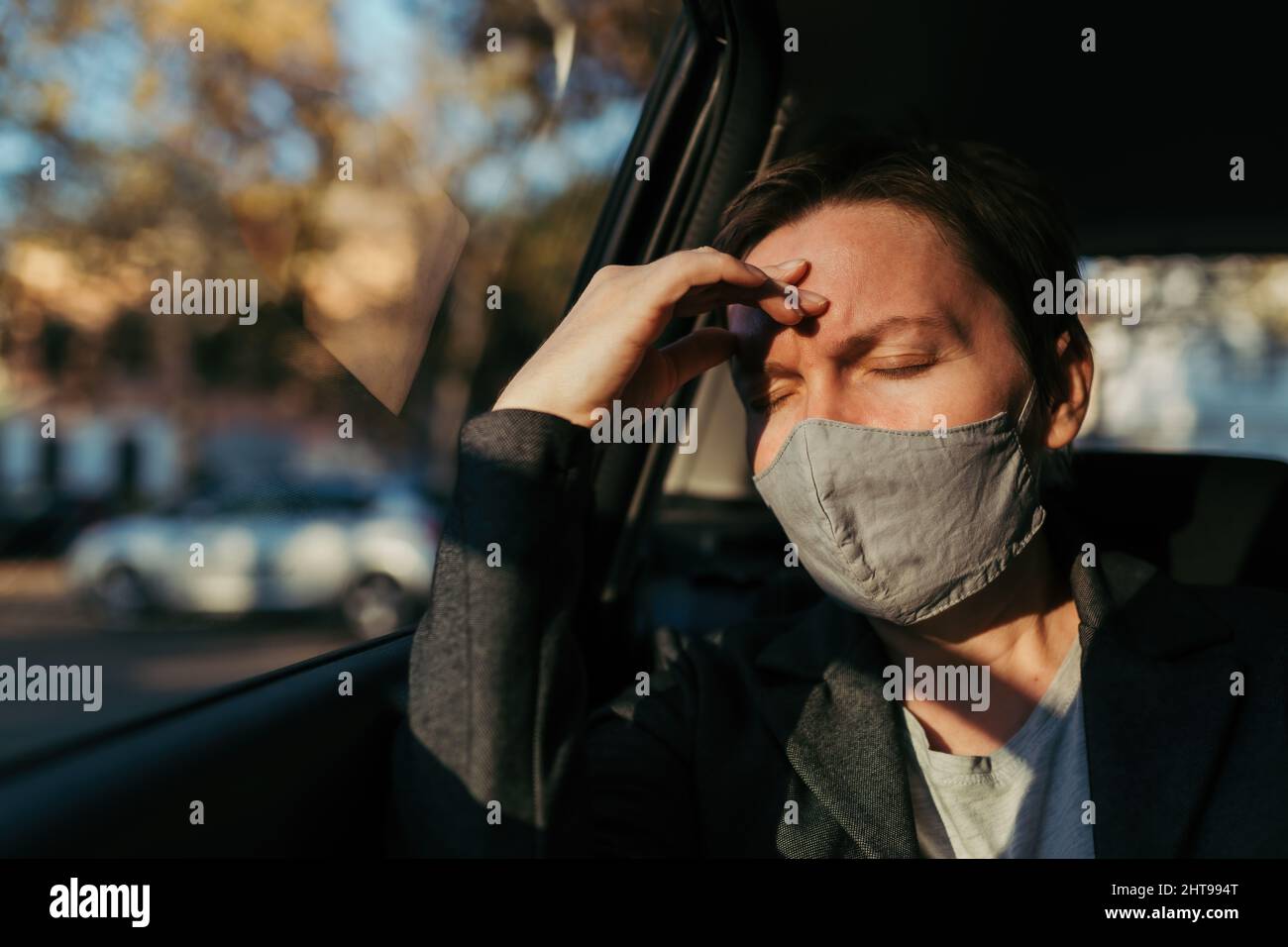 Geschäftsfrau mit starken Kopfschmerzen Schmerzsymptomen und schützender Gesichtsmaske auf dem Rücksitz eines Autos, selektiver Fokus Stockfoto