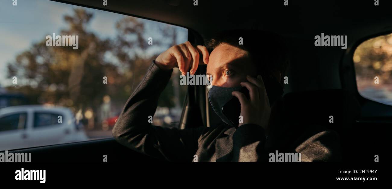 Seriöse Geschäftsfrau mit Schutzmaske, die auf dem Mobiltelefon vom Rücksitz des Autos aus spricht, selektiver Fokus Stockfoto