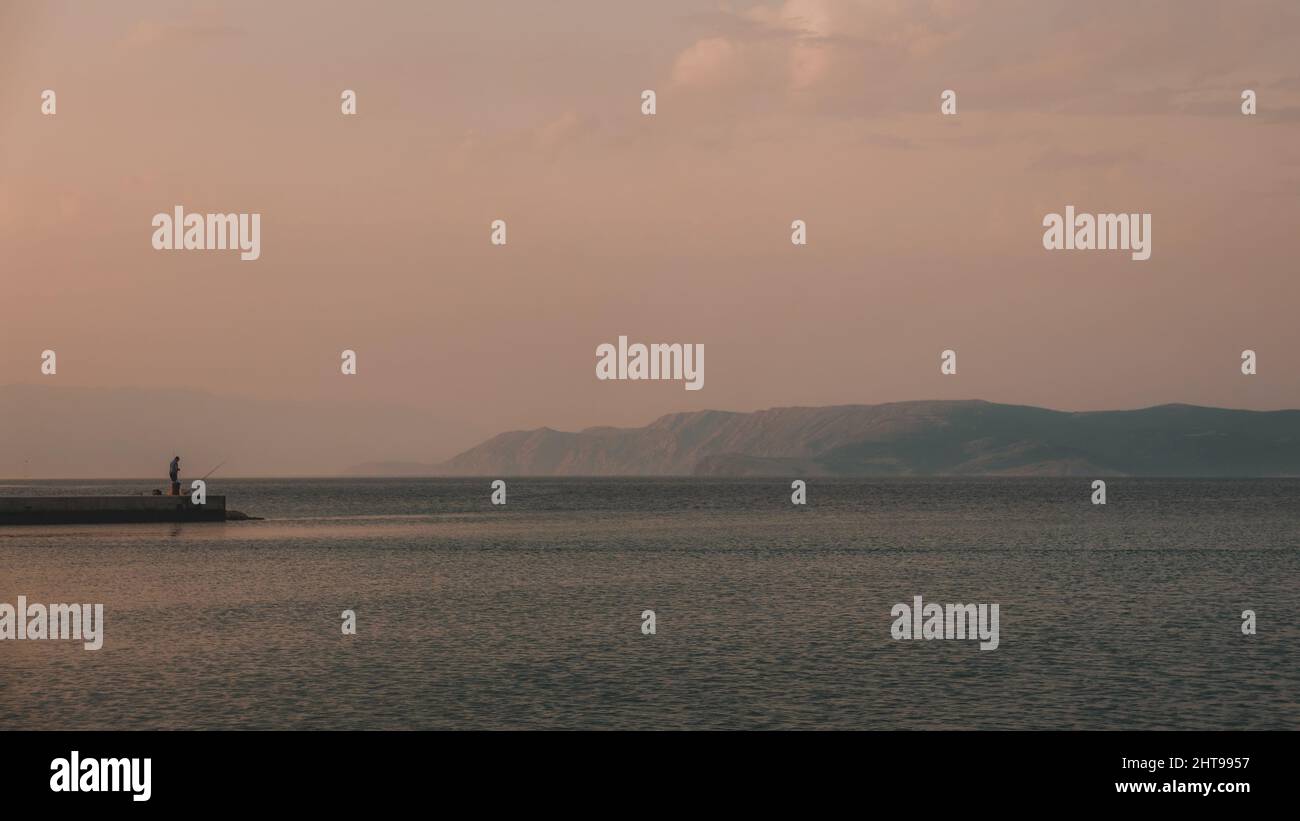 Allein Fischer stehen auf dem Dock und Angeln, Insel Krk im Hintergrund Stockfoto