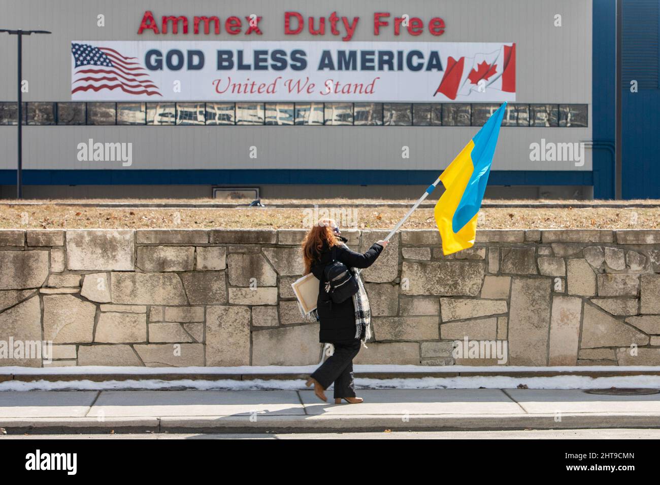 Detroit, Michigan, USA. 27.. Februar 2022. Eine Frau trägt eine ukrainische Flagge, als sie auf eine Kundgebung zugeht, die gegen die russische Invasion in der Ukraine protestiert. Fast 40.000 Einwohner von Michigan sind ukrainischer Abstammung. Kredit: Jim West/Alamy Live Nachrichten Stockfoto