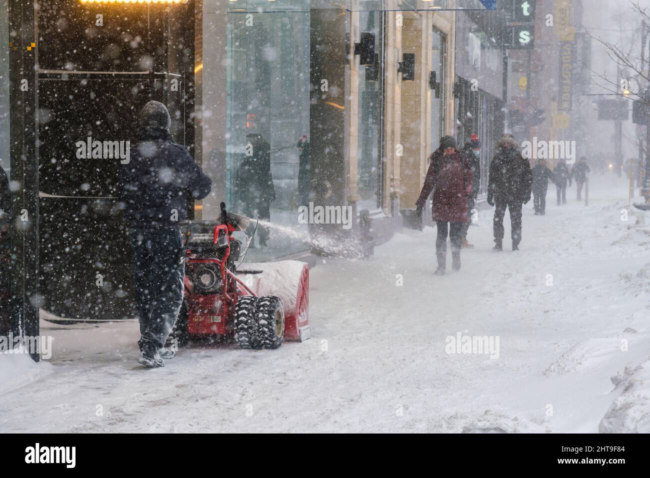 Montreal, KANADA - 25. Februar 2022: Mann schiebt Schnee mit einem Mini-Schneepflug auf der Sainte-Catherine Street Stockfoto