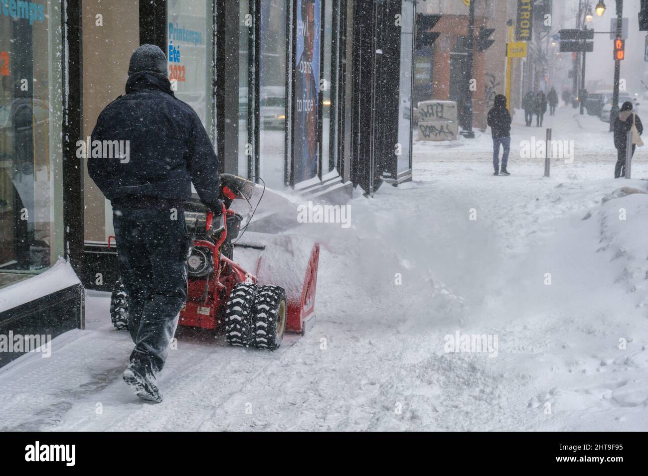 Montreal, KANADA - 25. Februar 2022: Mann schiebt Schnee mit einem Mini-Schneepflug auf der Sainte-Catherine Street Stockfoto
